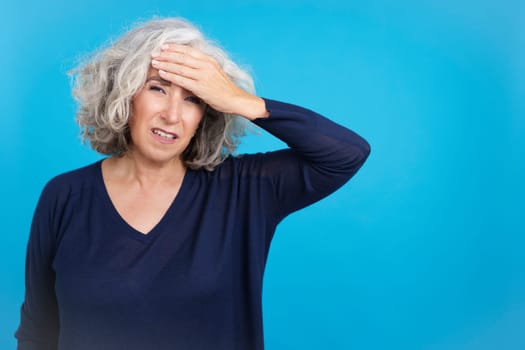 Studio portrait with blue background of a mature woman with a headache touching her forehead