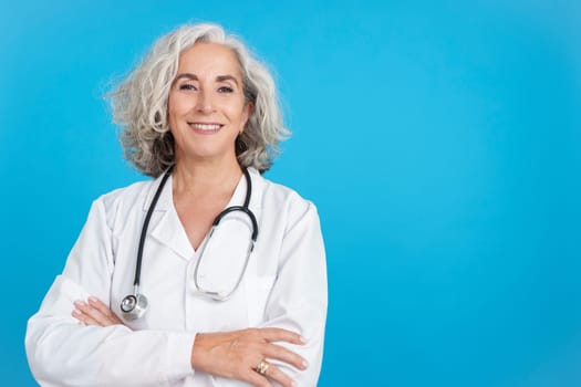 Studio portrait with blue background of a mature friendly doctor posing with a lab coat and a stethoscope while looking at the camera