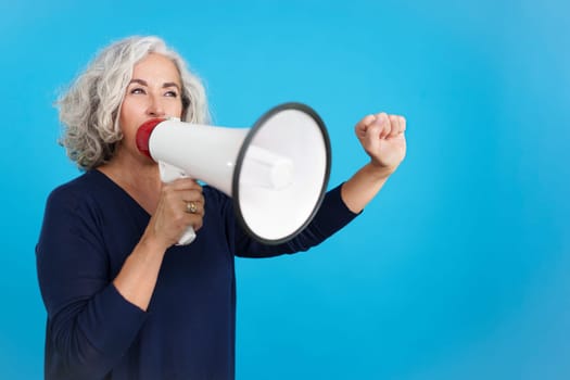 Studio portrait with blue background of an upset mature woman protesting with megaphone