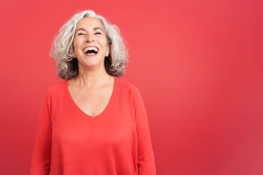 Studio portrait with red background of a mature woman in red shirt laughing while standing