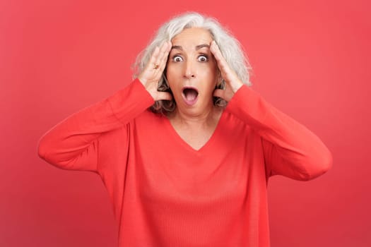 Studio portrait with red background of a mature woman gesturing with a surprised face with the mouth opened