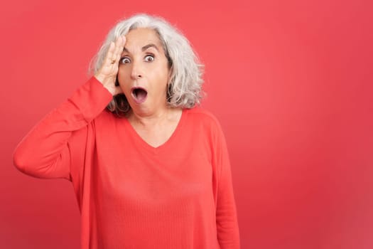 Studio portrait with red background of a mature woman looking at camera with a surprised look