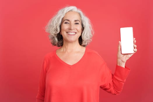 Studio portrait with red background of a mature woman showing the white screen of the mobile, Mock up