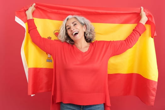 Studio portrait with red background of a happy mature woman raising a spanish national flag