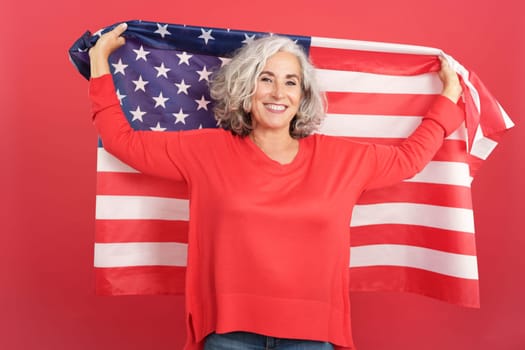 Studio portrait with red background of a happy mature woman raising a north america national flag