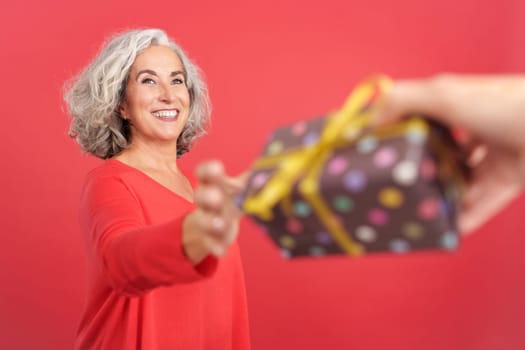 Studio portrait with red background of a happy mature woman receiving a gift