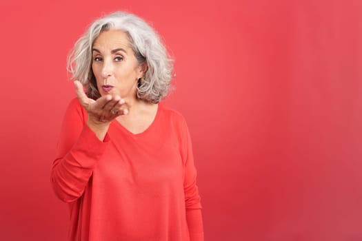 Studio portrait with red background of a mature woman blowing a kiss to the camera