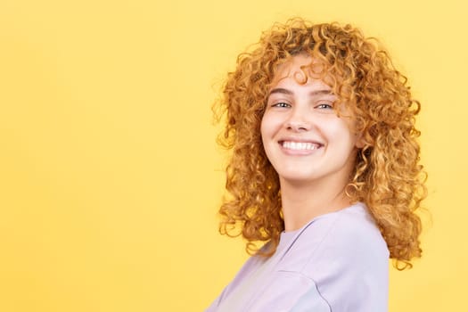 Studio image with yellow background of a beauty and happy woman with curly hair turning to smile at the camera