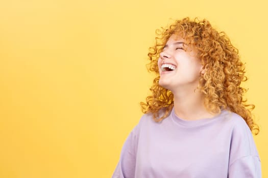 Studio image with yellow background of the profile of a beuty woman with curly hair and casual clothes laughing