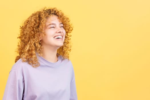 Studio image with yellow background of the profile of a happy woman with curly hair standing
