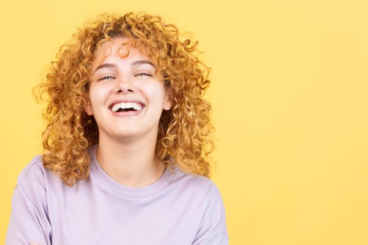 Studio image with yellow background of a beauty woman with curly hair looking at the camera while laughing