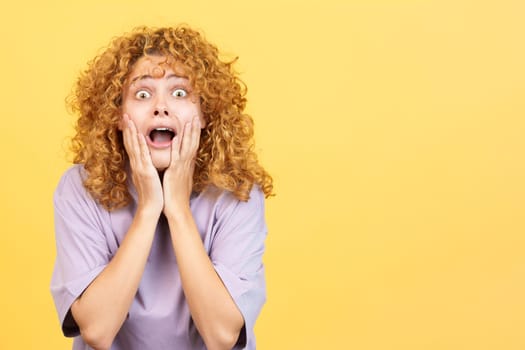 Studio image with yellow background of a beauty woman with curly hair gesturing with the hands on the face expressing dismay