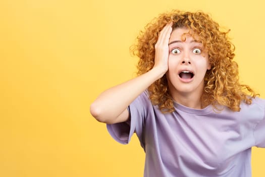 Studio image with yellow background of a woman with hand on head expressing dismay