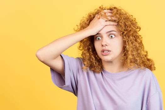 Studio image with yellow background of a woman with curly hair gesturing with the hand on head expressing desperation