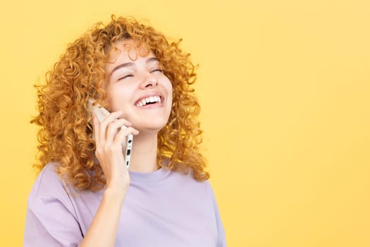 Studio image with yellow background of a beauty woman with curly hair talking to the mobile while smiling with eyes closed