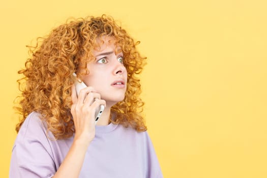 Studio image with yellow background of a frightened woman with curly hair talk to the mobile phone