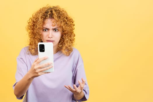 Studio image with yellow background of a upset and worried woman with curly hair using a mobile