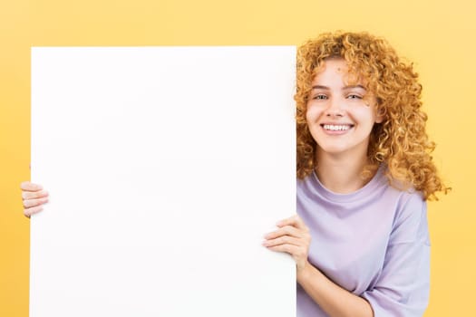Studio image with yellow background of a beauty smiley woman with curly hair holding a blank panel