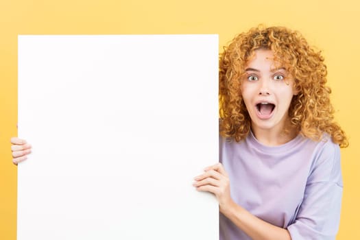 Studio image with yellow background of a beauty surprised woman with curly hair holding a blank board