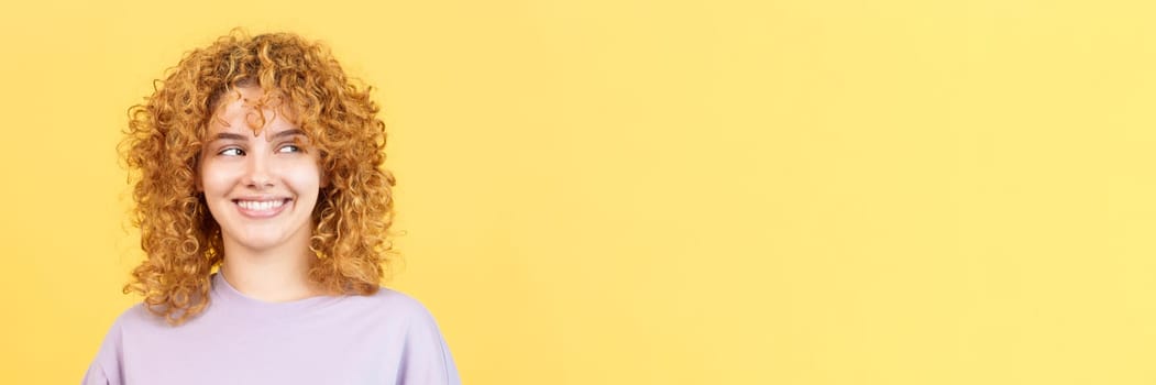 Panoramic studio image with yellow background of a happy beauty woman with curly hair looking aside