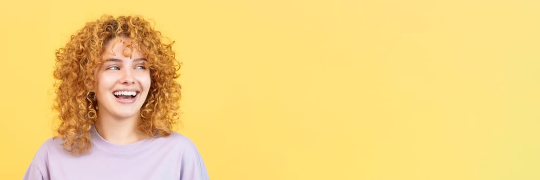 Panoramic studio image with yellow background of a smiley woman with curly hair looking aside