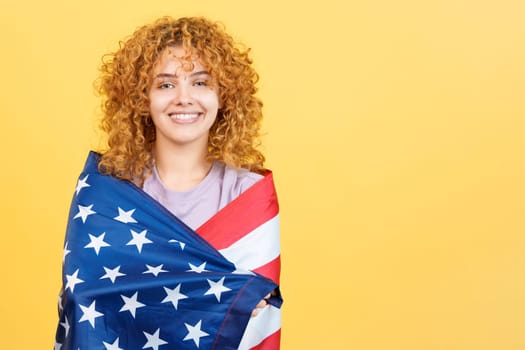Studio image with yellow background of a woman smiling at the camera while wrapping with a north america national flag