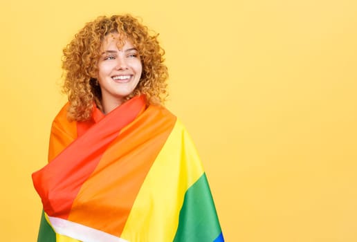 Studio image with yellow background of a smiley and distracted woman with curly hair wrapped with a lgbt flag