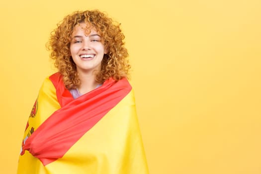 Studio image with yellow background of a beauty woman smiling at camera while wrapping with a spanish national flag