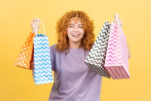 Studio image with yellow background of a happy woman smiling at the camera while showing shopping bags