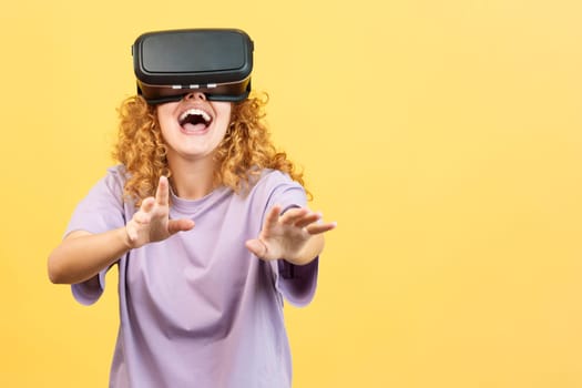 Studio image with yellow background of a surprised woman with curly hair and casual clothes smiling while using virtual reality goggles