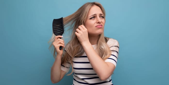 sad upset blond young woman with falling hair combing her hair on a blue background.