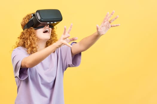 Studio image with yellow background of a young woman with curly hair gesturing while using a virtual reality goggles