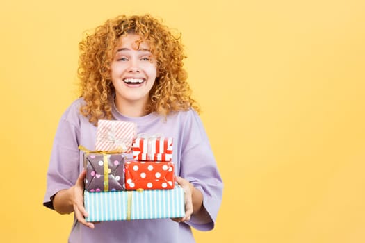 Studio image with yellow background of a emotional young woman smiling at the camera while receiving many gifts