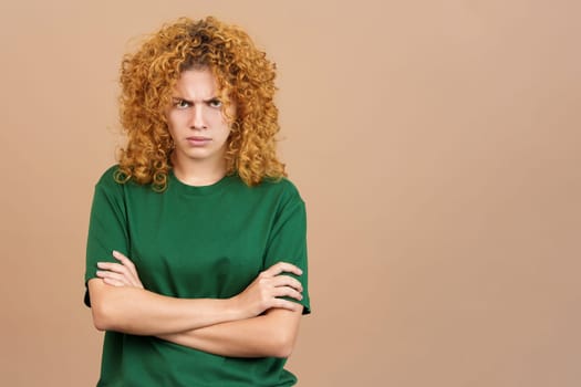 Studio image of a young woman with curly hair crossing the arms while looking at camera with an angry expression
