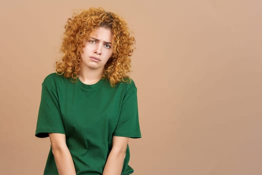 Studio image of a sad woman wit curly hair and casual clothes looking at the camera about to cry