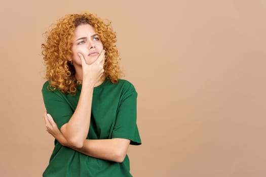 Studio image of a young woman with curly hair gesturing and looking up with doubtful expression
