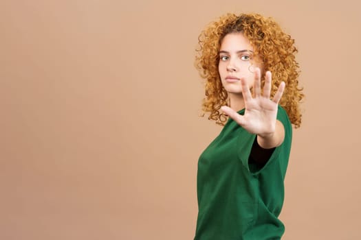 Studio image of a young serious woman with curly hair gesturing rejection with her hand