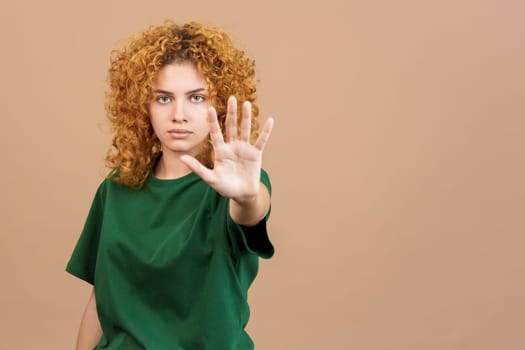 Studio image of a serious young woman with curly hair gesturing with her hand prohibition