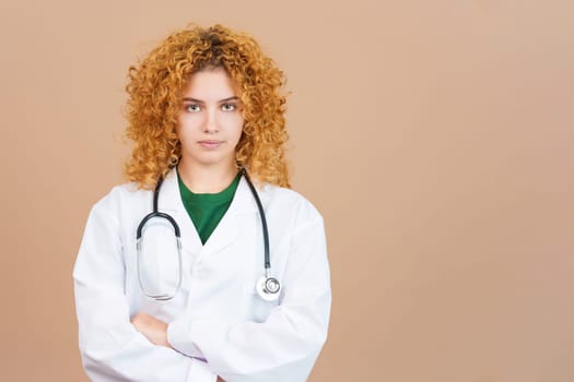 Studio image of a young serious female doctor with curly hair in lab coat with crossed arms