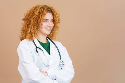 Studio image of a female doctor with curly hair smiling while looking aside with the arms crossed