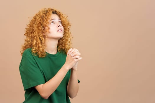 Studio image of a woman with curly hair looking up while praying with folded hands