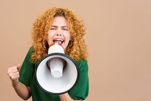 Studio image of a woman with curly hair looking at camera and shouting using a loudspeaker