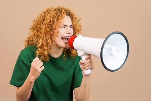 Studio image of an upset woman with curly hair shouting using a loudspeaker