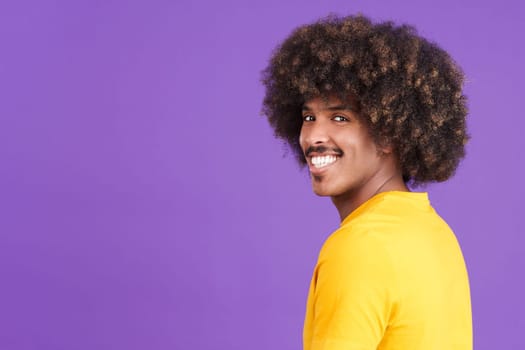 Happy african man with curly hair and casual clothing turning to smile at the camera in studio