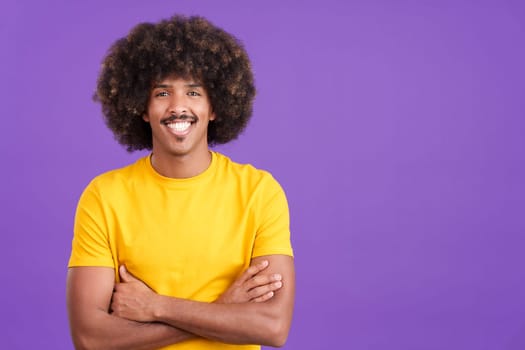 Happy cool african man with curly hair looking at camera with arms crossed in studio