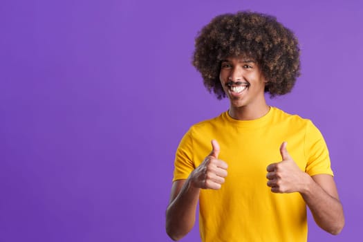 Smiling african man with curly hair gesturing agreement raising two thumbs up in studio