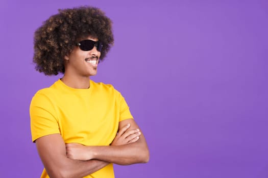 Smiley african man with curly hair wearing sunglasses posing with arms crossed in studio