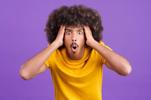Cool surprised african man with curly hair looking at the camera gesturing in studio