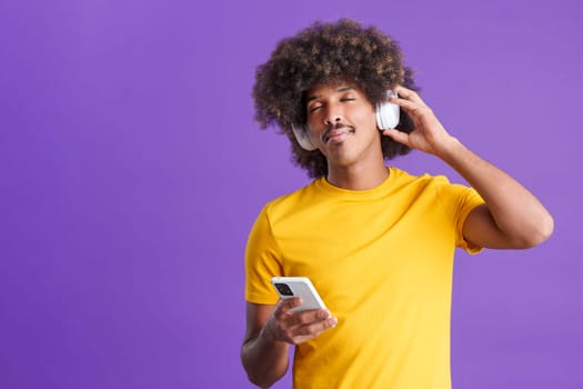 Cool african man relaxing while listening to music with headphones and the mobile in studio