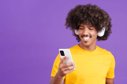 Stylish african man with curly hair listening to music with headphones and a mobile in studio